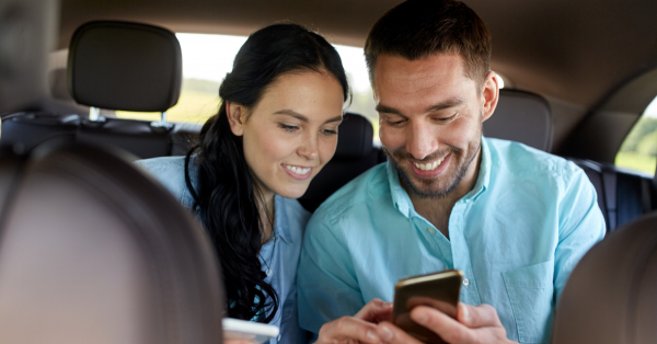 Man and Woman in back seat of car smiling while looking at one phone